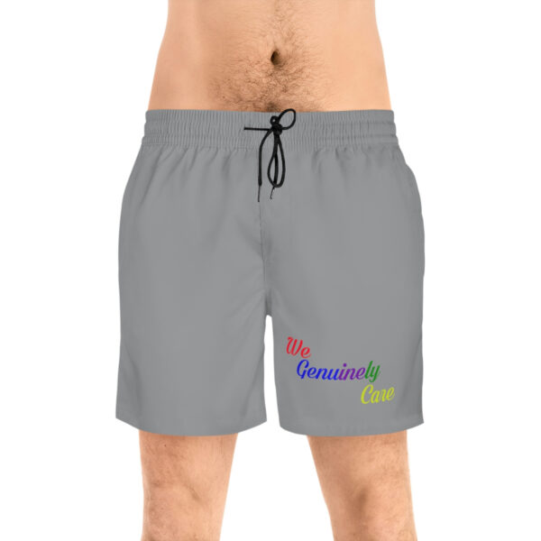 A man wearing grey swim trunks with the words " be beautiful " on it.